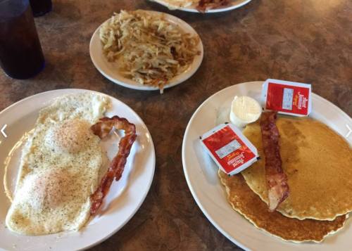 Two plates of breakfast: one with eggs, bacon, and hash browns; the other with pancakes and syrup.