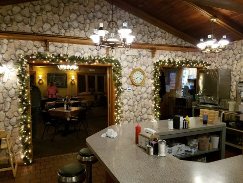 Cozy restaurant interior with stone walls, festive lights, and a counter view of tables and a kitchen area.