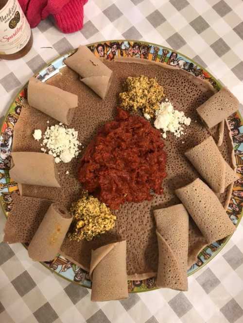 A colorful plate of injera with spicy red sauce and various toppings, arranged in a circular pattern.