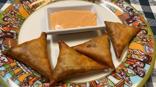 A plate with four golden-brown samosas and a small dish of dipping sauce.