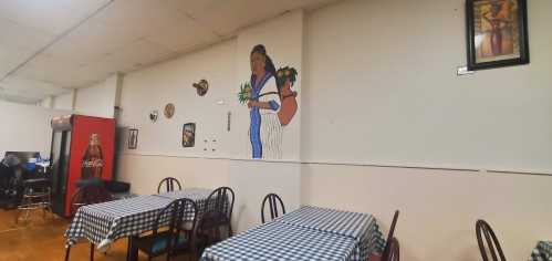 A cozy restaurant interior with checkered tables, wall art, and a mural of a woman holding flowers.