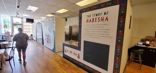 Interior of a restaurant featuring colorful murals and text about Habesha culture, with a person walking in the background.