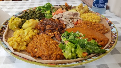 A colorful platter of Ethiopian food featuring injera, lentils, greens, and various vegetable dishes.