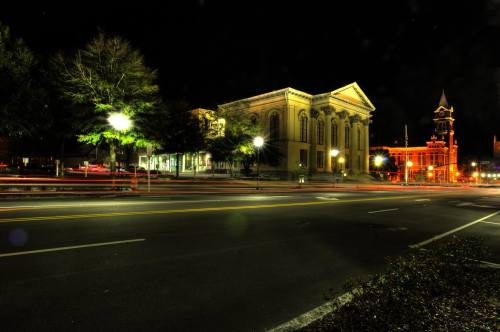 A nighttime city scene featuring historic buildings, streetlights, and light trails from passing cars.