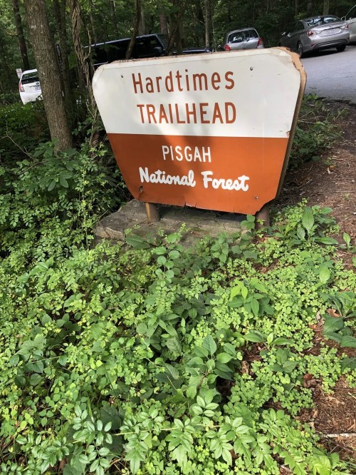 Sign for Hardtimes Trailhead in Pisgah National Forest, surrounded by greenery and trees.
