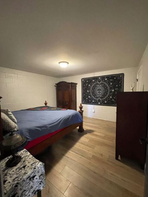 Cozy bedroom featuring a wooden bed, decorative tapestry, and wooden furniture on a light wood floor.