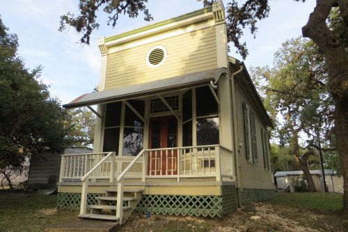 A charming yellow house with a porch, large windows, and a circular window, surrounded by trees.