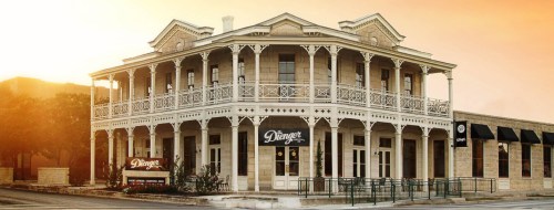 Historic building with a wraparound porch, featuring a sign for "Dienger" and a warm sunset backdrop.