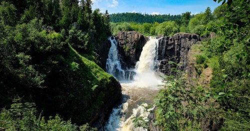 High Falls waterfall cascading over dark rocks into a river gorge at Grand Portage State Park, Minnesota.