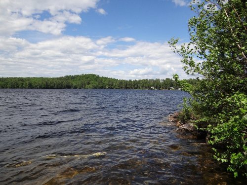 A serene lake surrounded by lush greenery and hills under a partly cloudy sky.