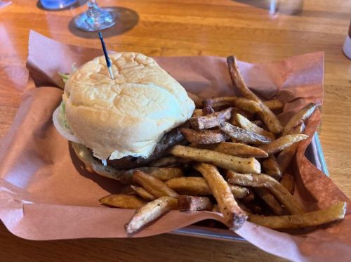 A burger with a toothpick on top, served with a side of crispy French fries in a basket.