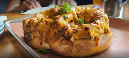 A cheesy, baked dish shaped like a ring, topped with green onions, on a metal tray with a blurred background.