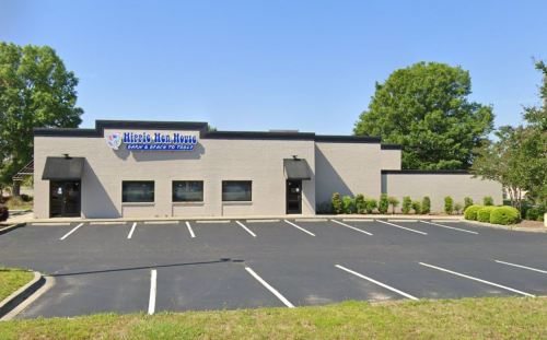 A single-story commercial building with a sign reading "Hippie Hen House," surrounded by a parking lot and trees.