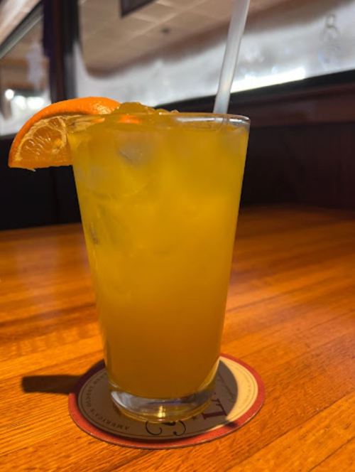 A refreshing orange drink with ice, garnished with a slice of orange, served in a clear glass on a wooden table.