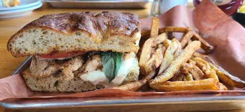 A sandwich with grilled chicken, tomato, and basil on rustic bread, served with crispy fries on the side.