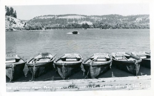 Black and white photo of boats lined up on a shore, with a river and distant hills in the background.