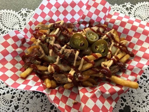 A basket of loaded fries topped with pulled meat, jalapeños, and drizzled with barbecue and creamy sauces.