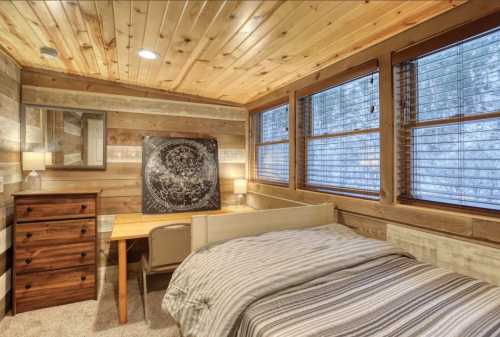 Cozy bedroom with wooden walls, a bed, desk, and large windows letting in natural light.