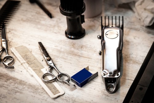 A collection of hairdressing tools including scissors, combs, and a clipper on a wooden surface.