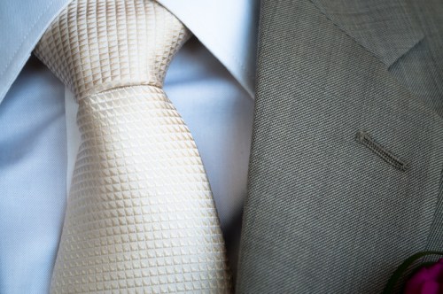 Close-up of a light-colored tie and a gray suit jacket with a lapel pin, set against a white shirt.