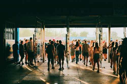 A crowd of people exiting a venue, illuminated by warm light, creating a lively festival atmosphere.