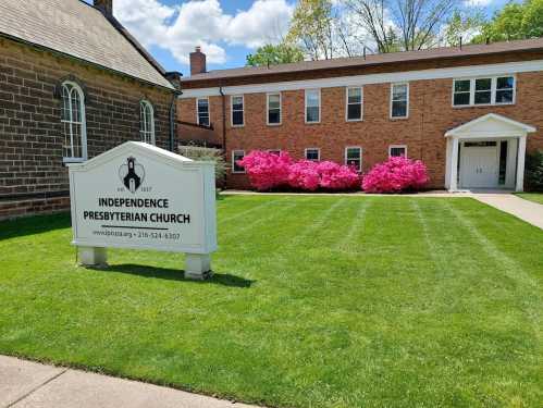 A well-maintained church building with a sign, surrounded by vibrant pink flowers and green grass on a sunny day.