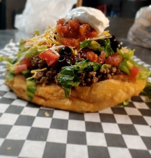 A delicious taco salad on a crispy shell, topped with seasoned beef, lettuce, tomatoes, cheese, black olives, and sour cream.