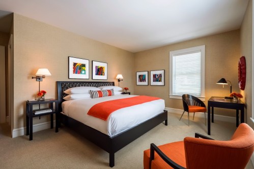 A modern hotel room featuring a large bed, artwork on the walls, a desk, and a cozy armchair.