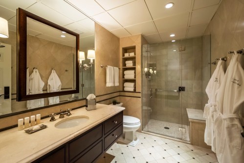 Luxurious bathroom featuring a glass shower, marble countertop, and neatly arranged towels and robes.