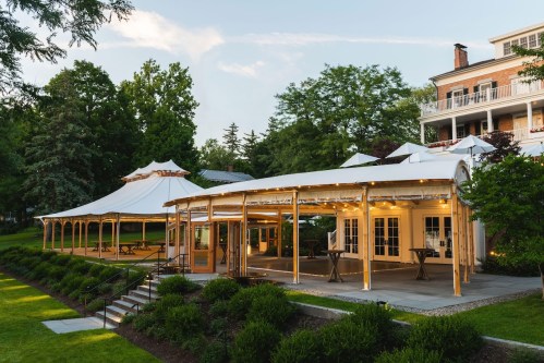 A spacious outdoor venue with a tent and a modern building, surrounded by lush greenery and trees.