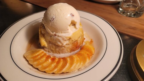 A dessert featuring a warm cake topped with vanilla ice cream and caramel sauce, accompanied by sliced caramelized bananas.