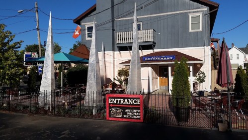 A restaurant with a sign reading "Entrance" and outdoor seating, surrounded by tall, pointed sculptures.