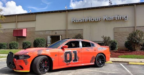 An orange car with the number 01 parked outside RushHour Karting, featuring a sporty design and black wheels.