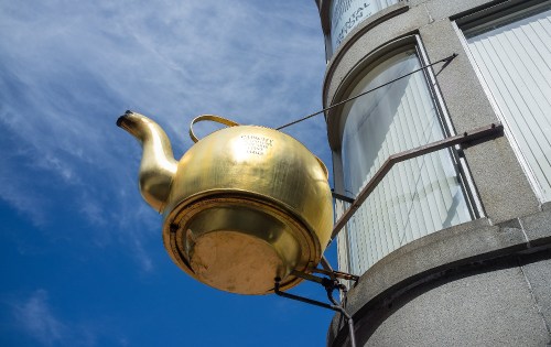 A large, shiny golden teapot sculpture mounted on a building against a blue sky.