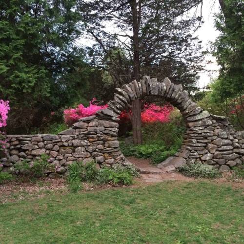 A stone archway surrounded by lush greenery and vibrant pink flowers in a serene garden setting.