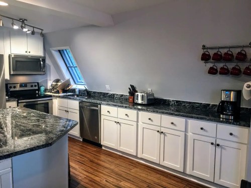 Modern kitchen with white cabinets, granite countertops, stainless steel appliances, and a coffee maker.