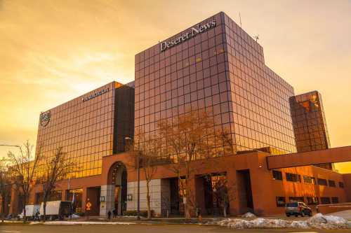 Sunset view of the Deseret News building, featuring modern architecture and reflective glass windows.