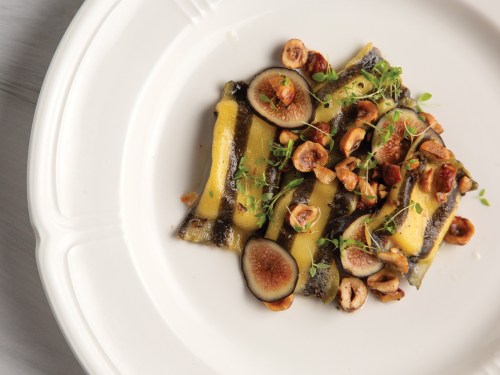 A plate of pasta with a yellow sauce, topped with figs, hazelnuts, and fresh herbs.