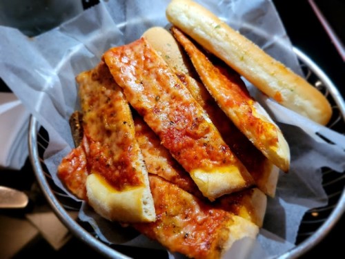 A basket of crispy flatbread topped with marinara sauce, alongside soft breadsticks.