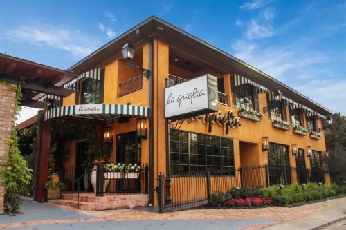 Exterior of La Gagita restaurant featuring a warm orange facade, striped awnings, and lush greenery.