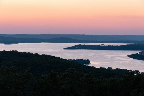 A serene landscape at sunset, featuring a calm lake surrounded by hills and a colorful sky.