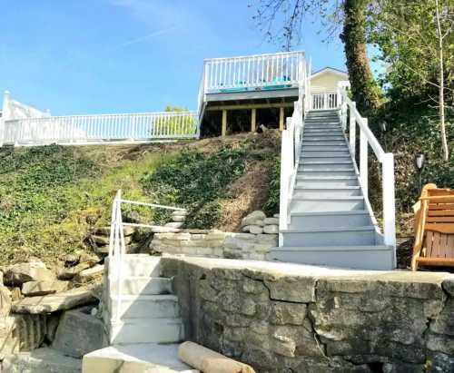 A set of white stairs leads up a hillside, surrounded by greenery, with a deck visible at the top.