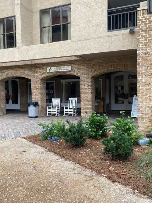 A building entrance with rocking chairs, potted plants, and a sign for "Pure Bar Studio" visible.