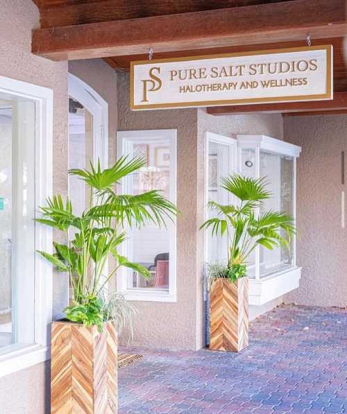 Exterior of Pure Salt Studios, featuring a sign for halotherapy and wellness, with potted plants by the entrance.