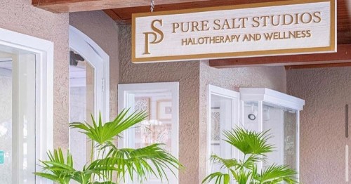 Sign for Pure Salt Studios, featuring "Halotherapy and Wellness," surrounded by indoor plants.