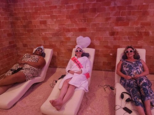 Three people relax on lounge chairs in a spa-like setting, wearing sunglasses and enjoying a calm atmosphere.