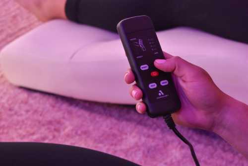 A hand holding a remote control with various buttons, resting on a soft surface.