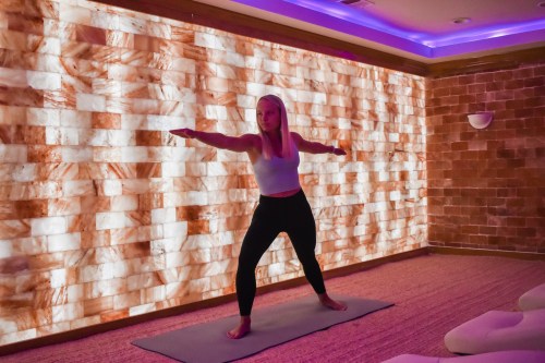 A person practicing yoga in a serene space with a glowing salt wall, striking a warrior pose on a mat.