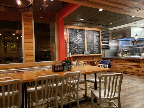 Cozy restaurant interior with wooden walls, empty tables, and a chalkboard menu in the background.