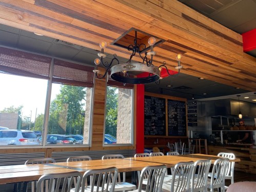 Interior of a restaurant featuring wooden walls, a chandelier, and a large communal table with metal chairs.